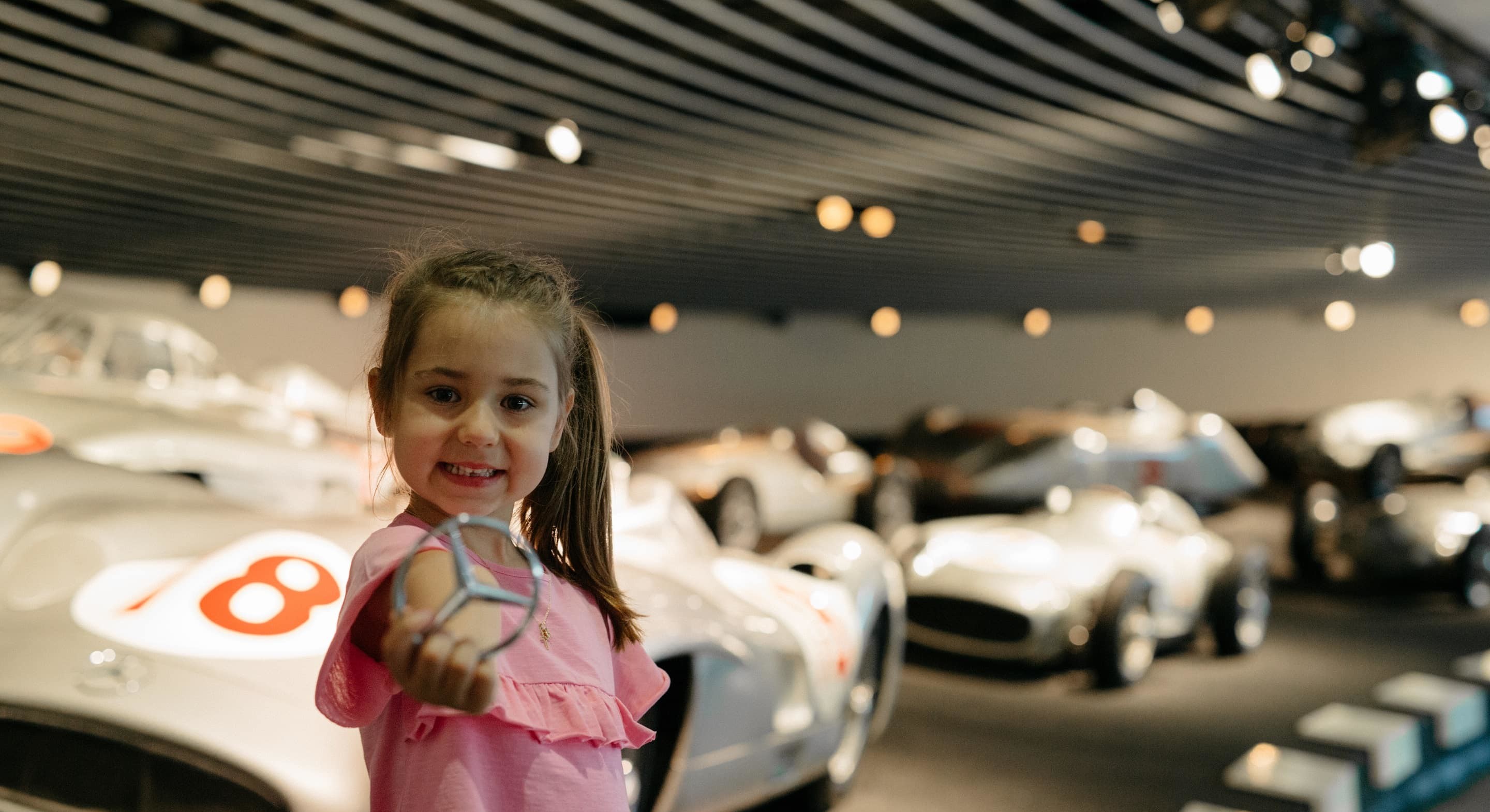 Ein Mädchen steht vor den Rennwagen und hält einen Mercedesstern in der Hand.