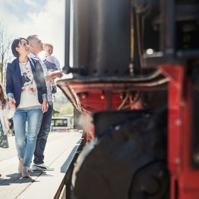 Eine Familie steht neben einer schwarzen Lokomotive auf dem Bahnsteig.