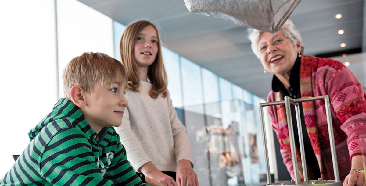 Zwei Kinder und eine Frau testen eine Experimentierstation zu physikalischen Grundlagen der Luftschifftechnik.