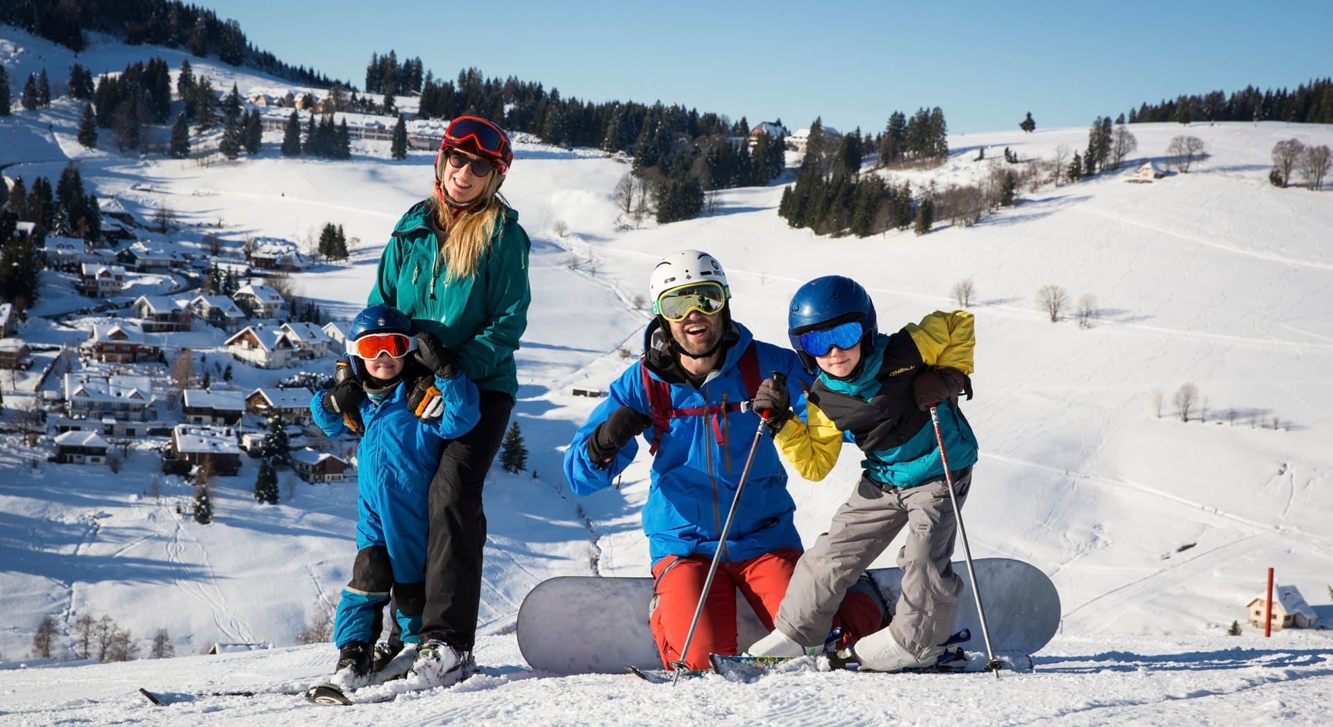 Eine Familie mit Skiern und Snowboard steht in der Winterlandschaft.