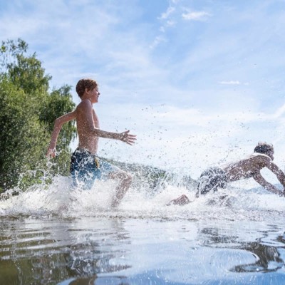 Zwei Jungs rennen in den Schluchsee und springen ins Wasser.