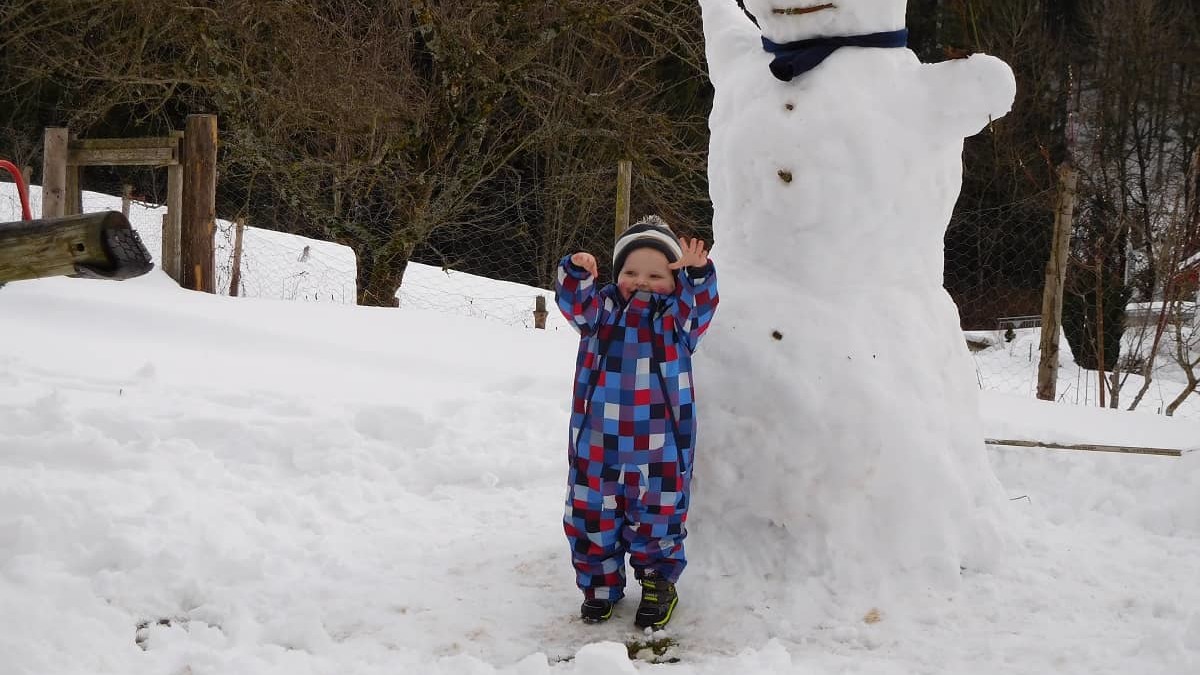 Ein kleines Kind steht im Schnee neben einem großen Schneemann.