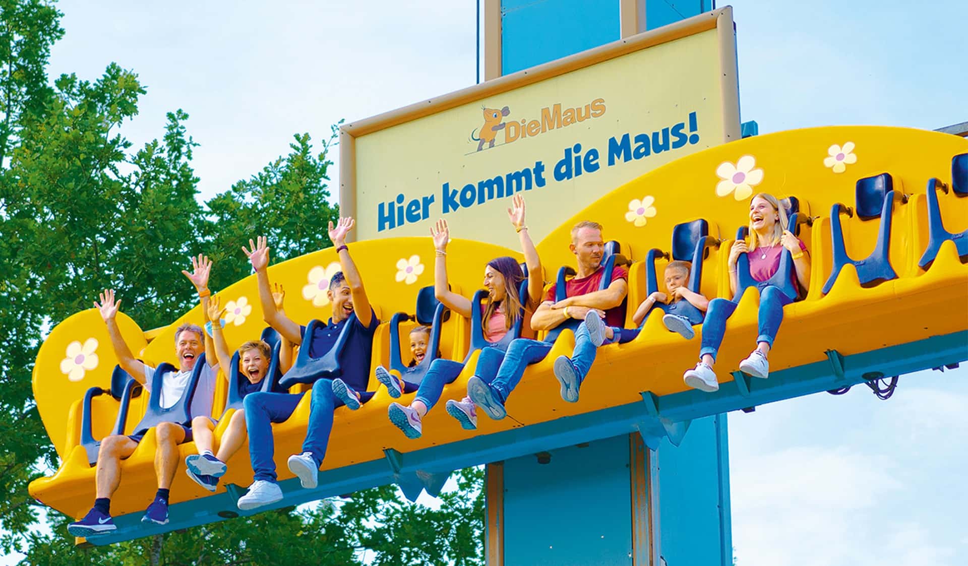 Lachende Familien mit den Händen in der Luft im orangefarbenen Freifallturm.