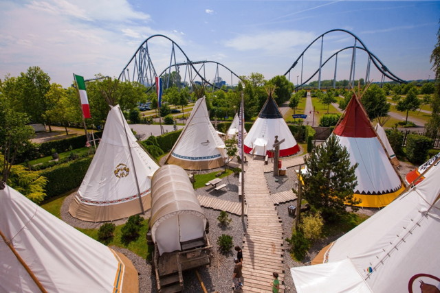 Blick auf das Camp-Resort mit Tipi-Zelten und einem Planwagen. Im Hintergrund sind Achterbahnen zu sehen.