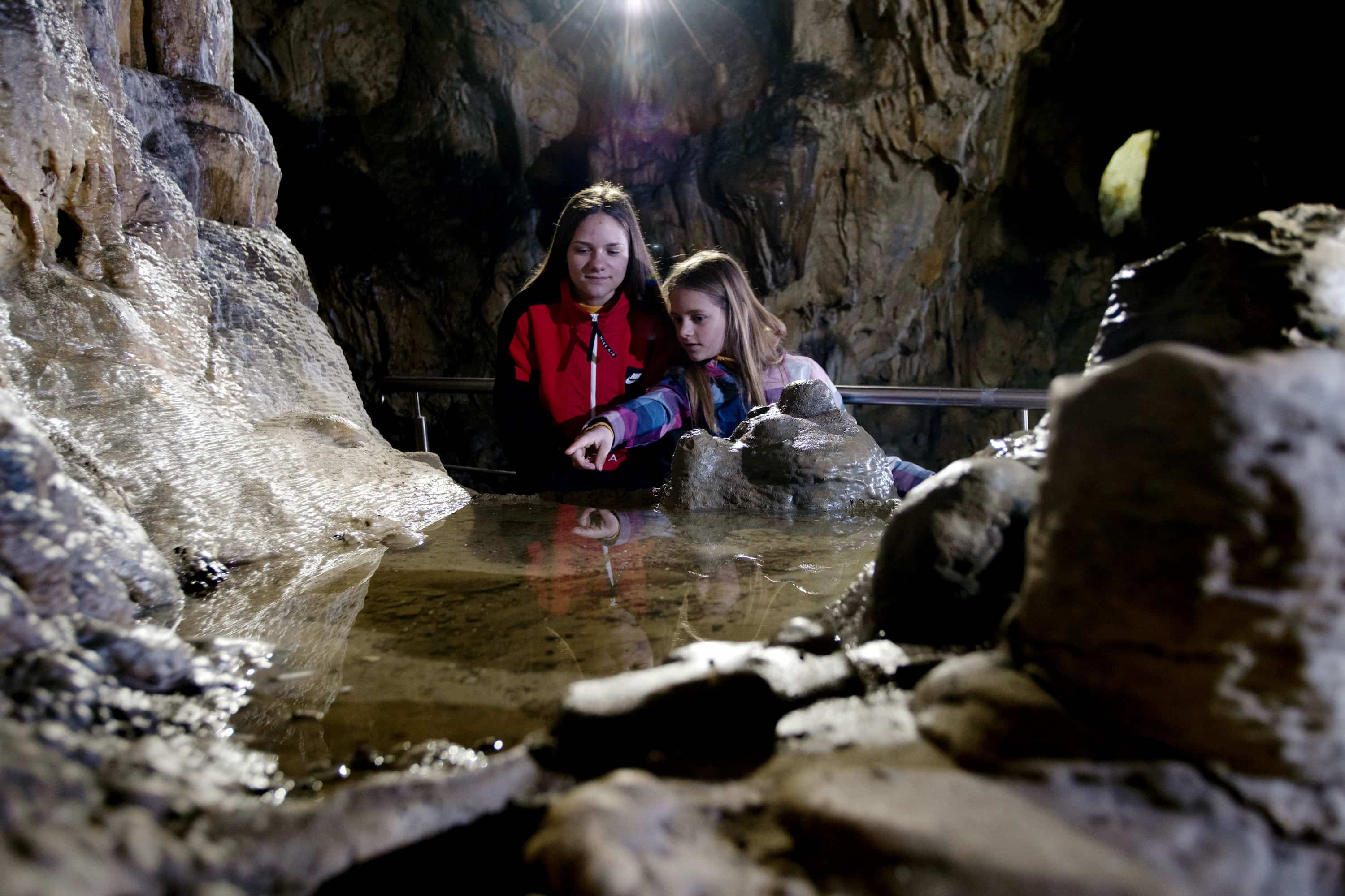 Zwei Mädchen schauen in der Charlottenhöhle in ein Tropfsteinbecken mit Wasser.