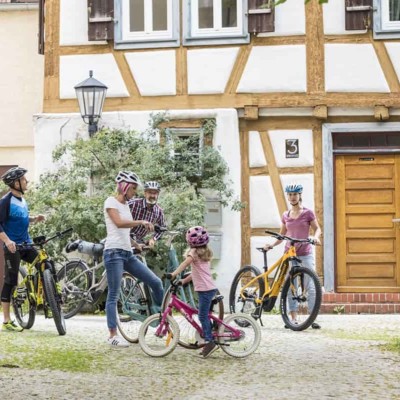 Eine Familie steht mit den Fahrrädern vor einem Fachwerkhaus.