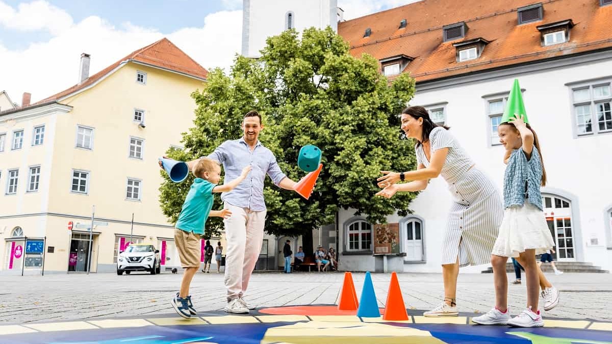 Eine Familie spielt "Fang den Hut" auf dem großen Spielteppich in Ravensburg.