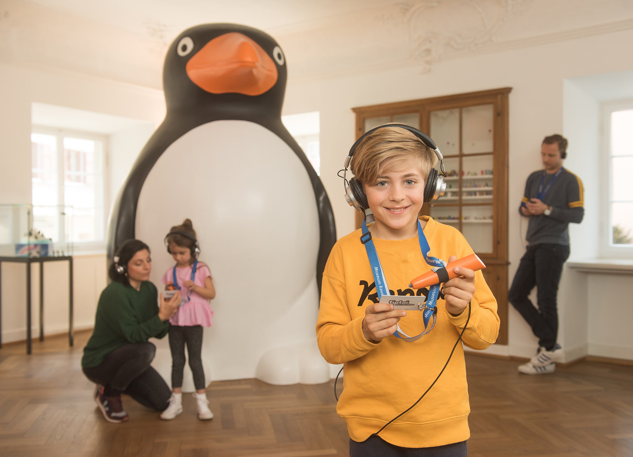 Ein Junge steht mit einen tiptoi-Stift vor einem überdimensionalem Pinguin.