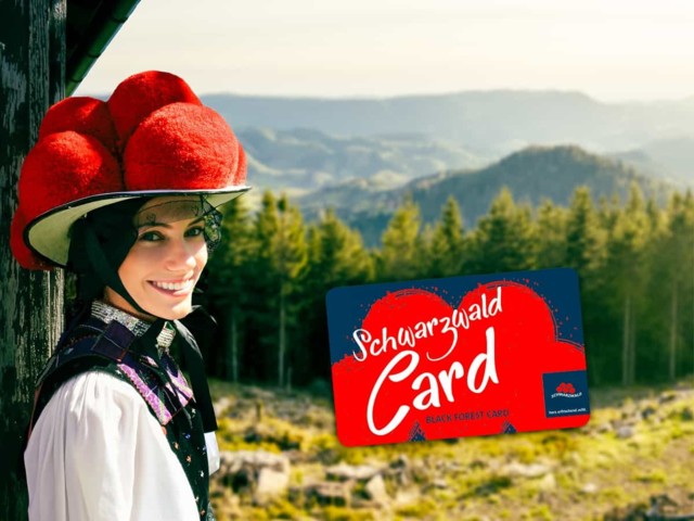 Eine junge Frau in Schwarzwälder Tracht und mit rotem Bollenhut steht vor Schwarzwaldlandschaft und lächelt in die Kamera. Die SchwarzwaldCard ist eingeblendet.
