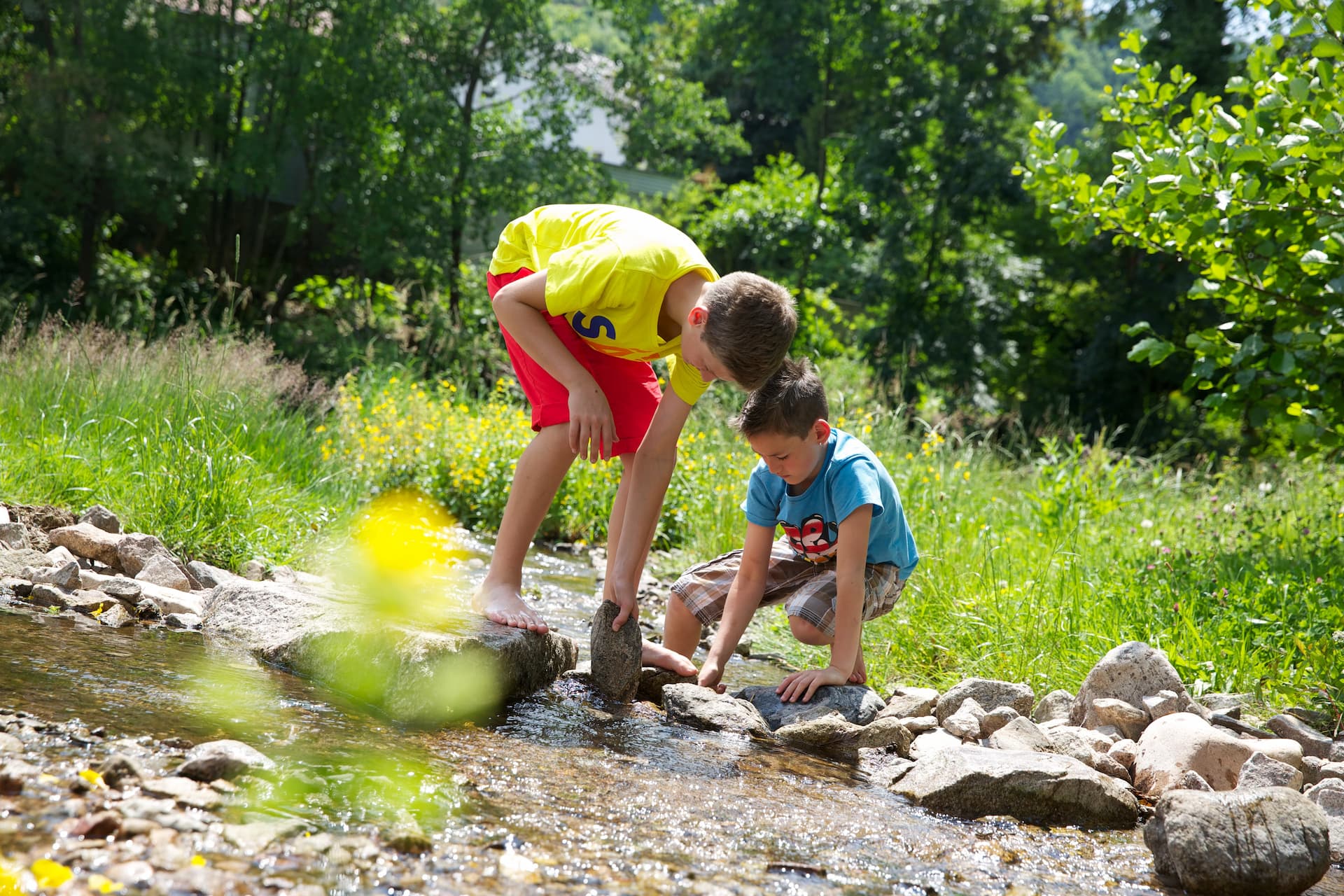 Kinder am Bach bauen einen Staudamm aus Steinen 