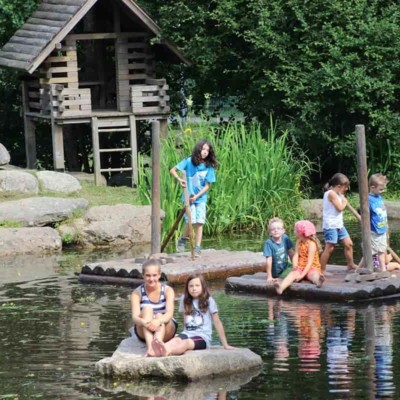 Kinder schwimmen auf Holzflößen über den Teich bei Tannis Tierscheune in Unterkirnach.