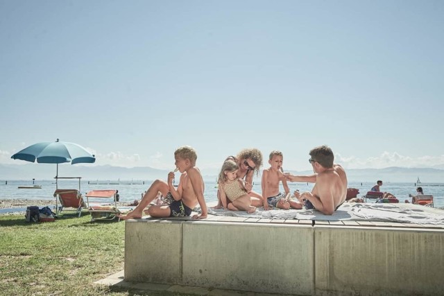 Familie liegt auf dem Liegepodest am Bodenseestrand und isst Eis.