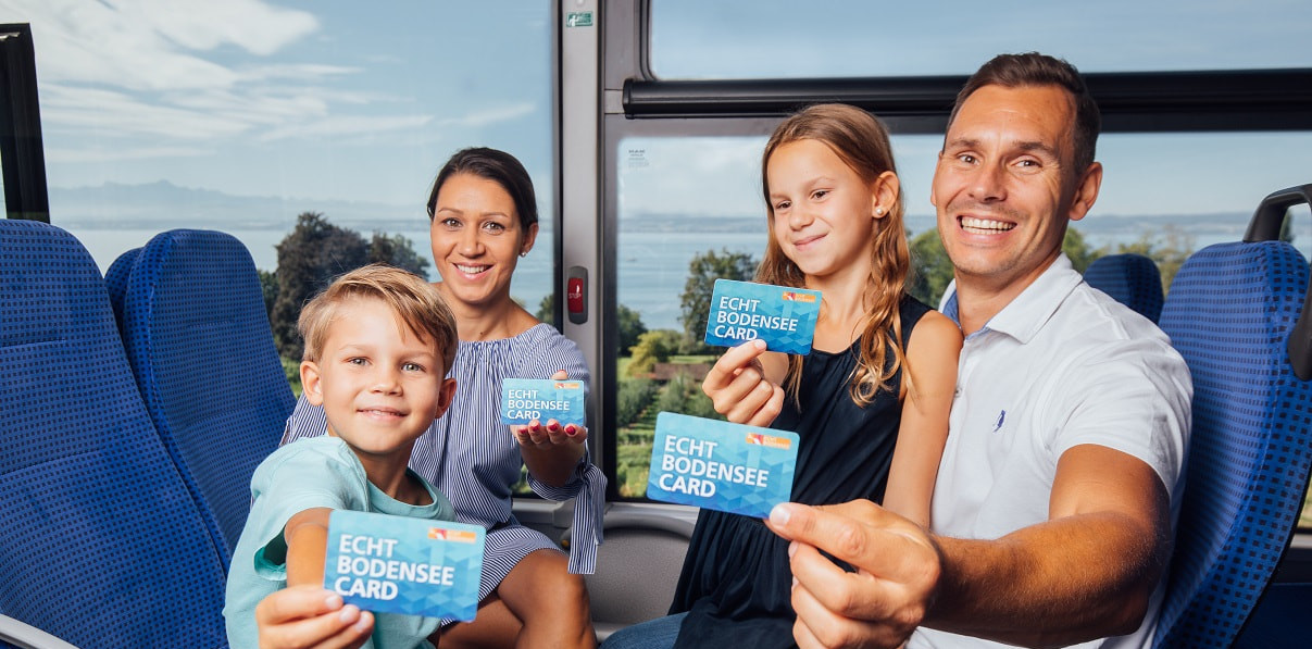 Eine Familie sitzt in einer Bahn und fährt am Bodensee entlang. Alle halten eine Echr Bodensee Card in der Hand.