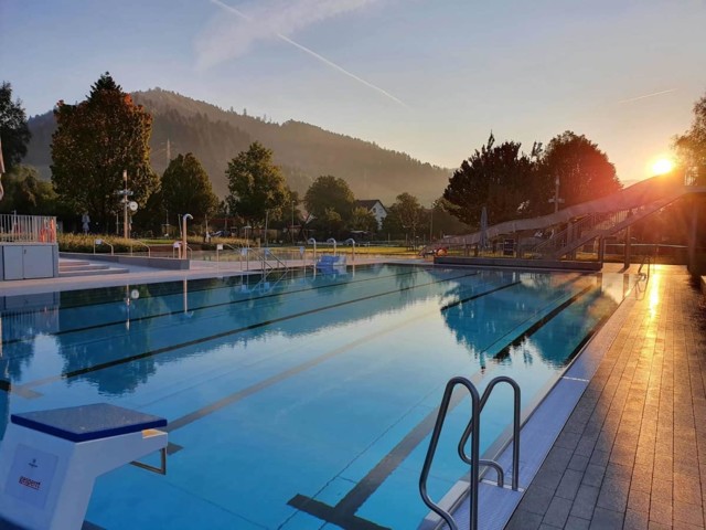 Leeres Schwimmbad, die aufgehende Morgensonne spiegelt sich im Wasser